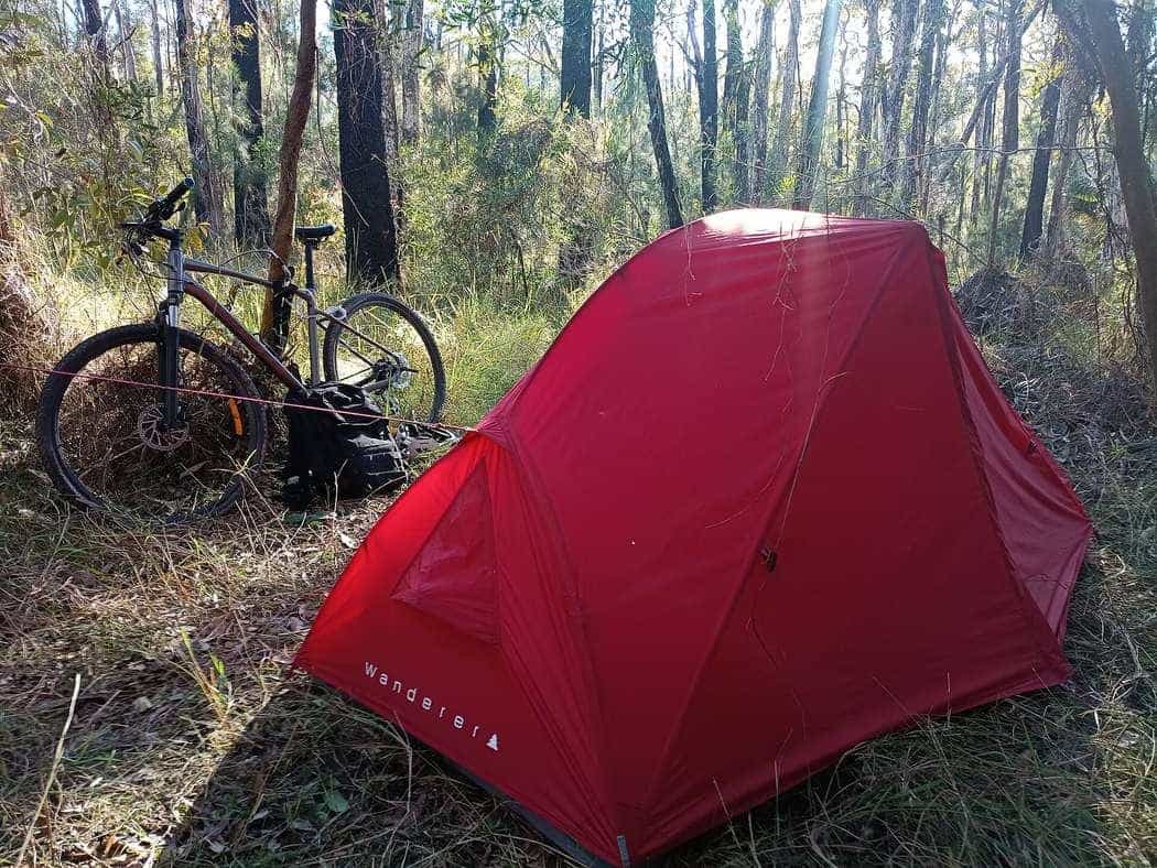 A loaded hybrid touring bicycle leaning beside a small tent in Australian bushland